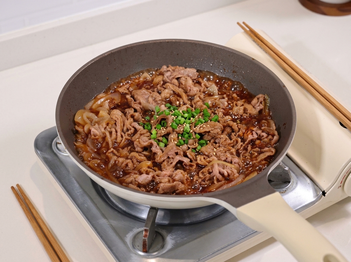 De fines tranches de bœuf et des oignons mijotant dans une sauce soja sombre et sirupeuse dans une poêle.