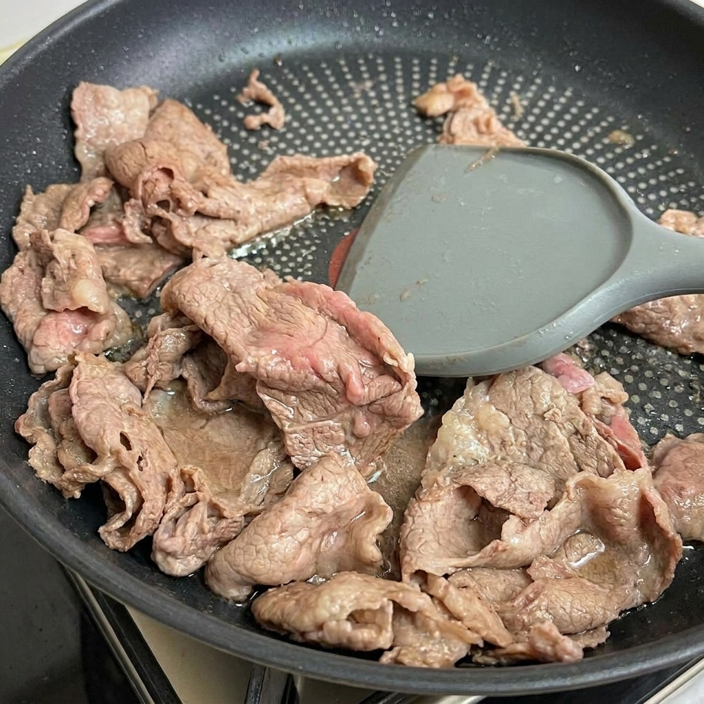 Spatule soulevant le bœuf à peine cuit de la poêle.