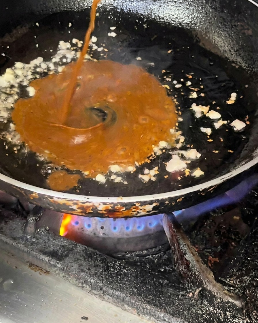 Sauce sombre versée dans une poêle contenant lail et loignon sautés.