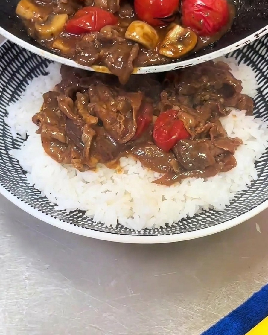 Le mélange de bœuf, champignons et tomates versé sur le lit de riz blanc.