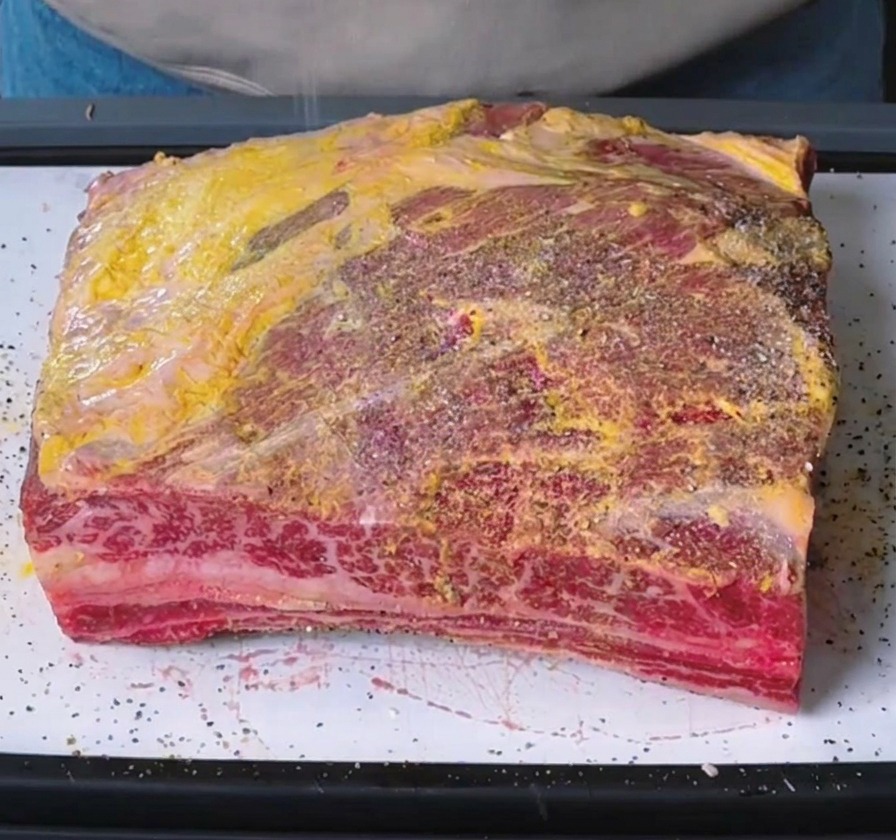 Saupoudrage de sel et de poivre noir concassé sur les côtes de bœuf badigeonnées de moutarde.
