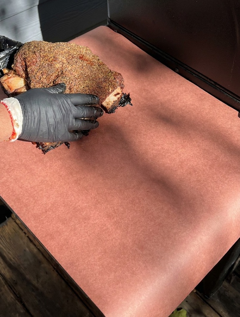 Mains gantées déposant les côtes fumées sur une grande feuille de papier de boucher rose.
