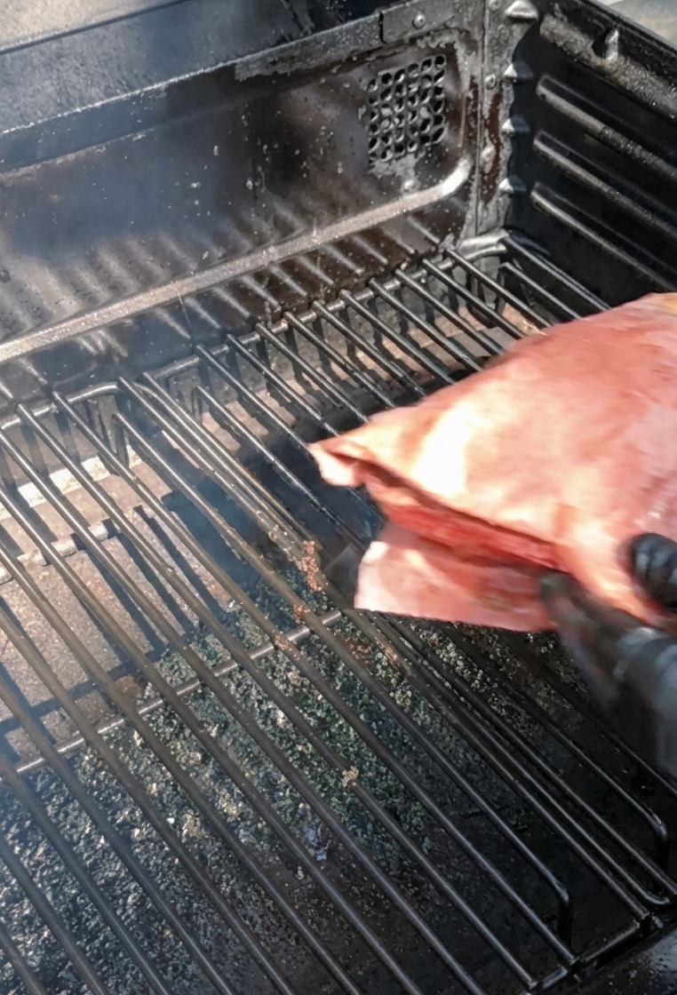 Personne avec des gants noirs plaçant le paquet en papier rose sur les grilles du fumoir.