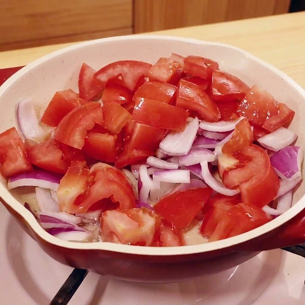 Tomates et oignons rouges hachés cuisant dans une poêle.