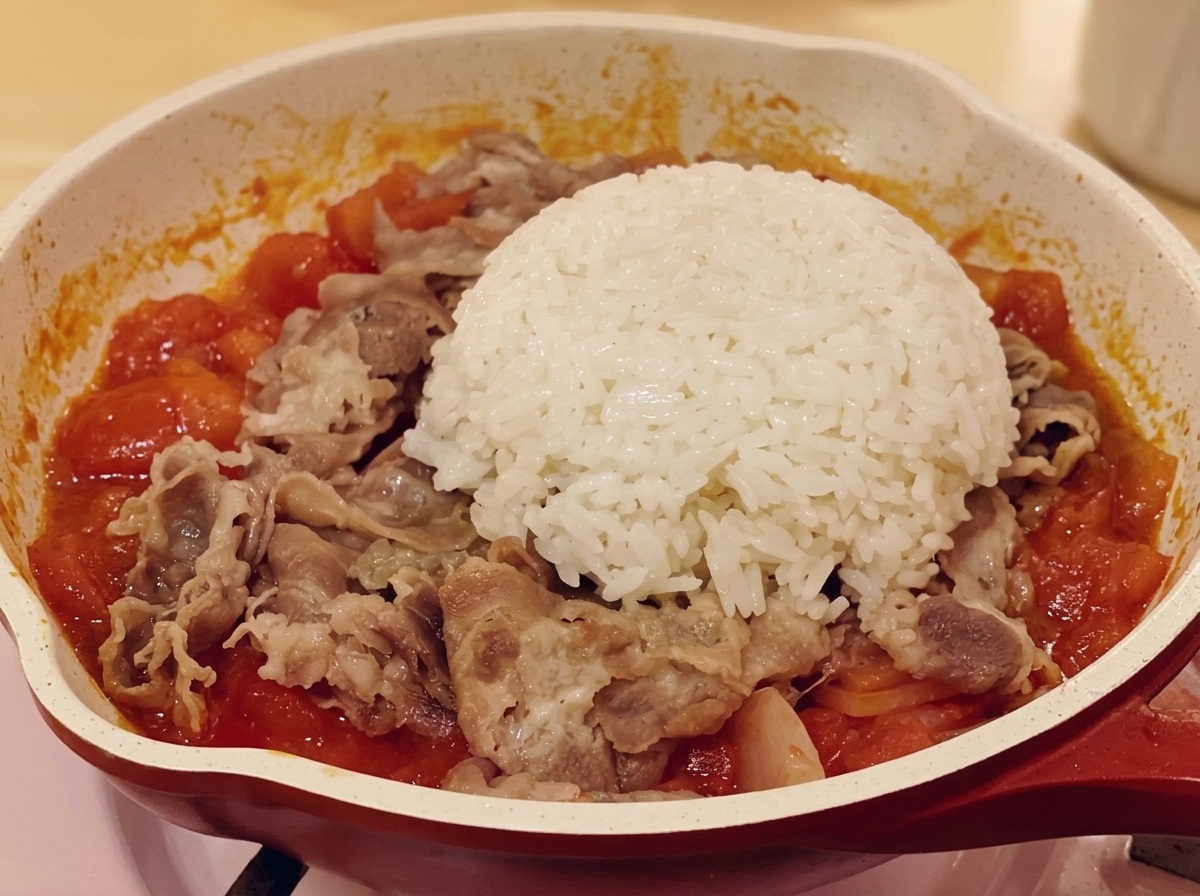 Un dôme de riz blanc posé sur le mélange de bœuf et de tomates dans une poêle.