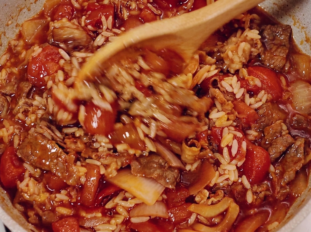 Une cuillère en bois mélangeant le bœuf, le riz et la sauce tomate dans une poêle.