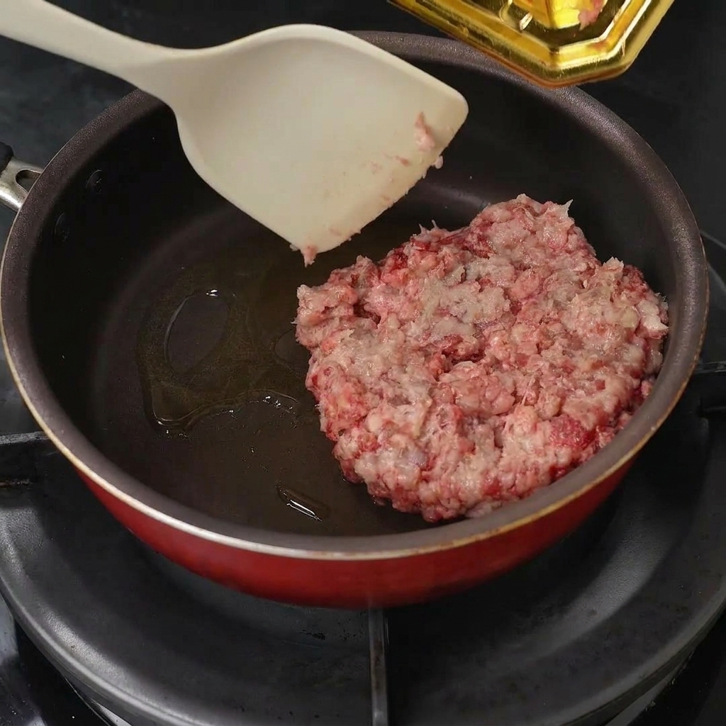 Du bœuf haché placé dans une poêle huilée et émietté avec une spatule.