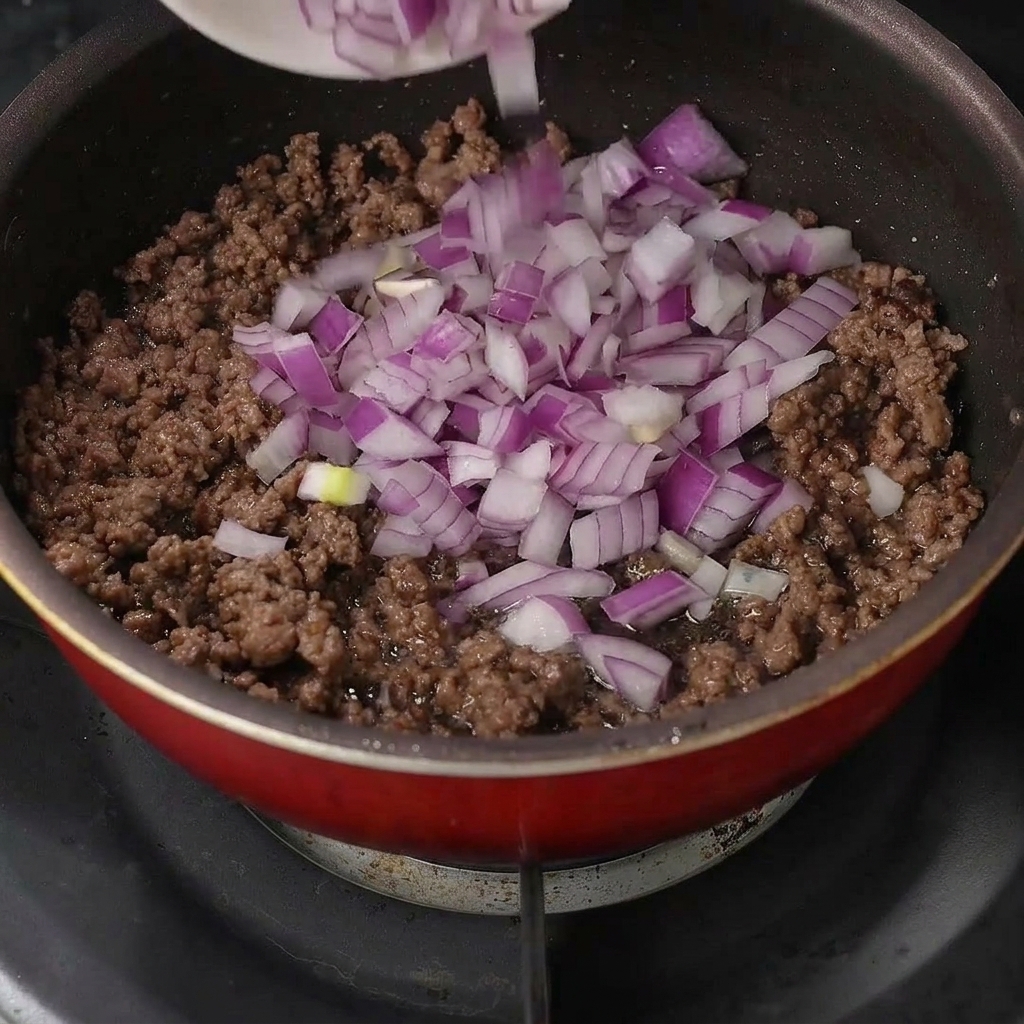 Des dés doignon rouge frais versés sur le bœuf haché cuit dans une poêle.