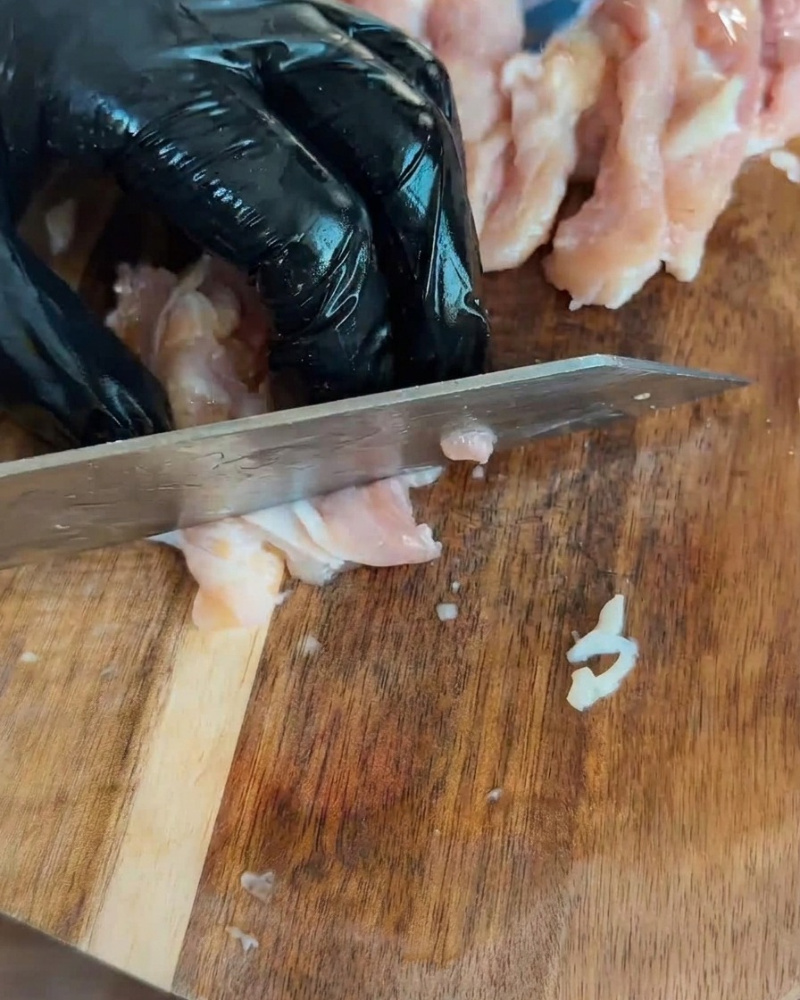 Morceaux de poulet cru coupés en dés sur une planche à découper en bois.