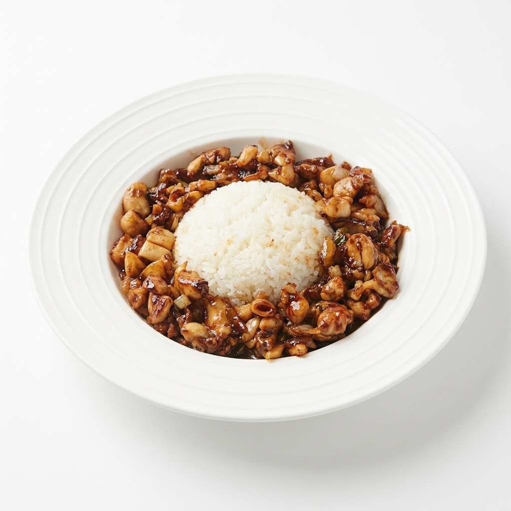 Poulet sauté laqué disposé autour du monticule de riz sur une assiette blanche.