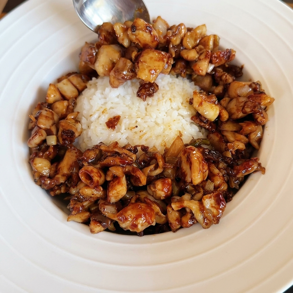 Un œuf au plat parfaitement cuit déposé sur un bol de riz et poulet sauté.