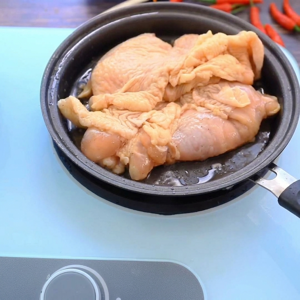 Hauts de cuisse de poulet dorant dans une poêle chaude, montrant une surface dorée et croustillante.