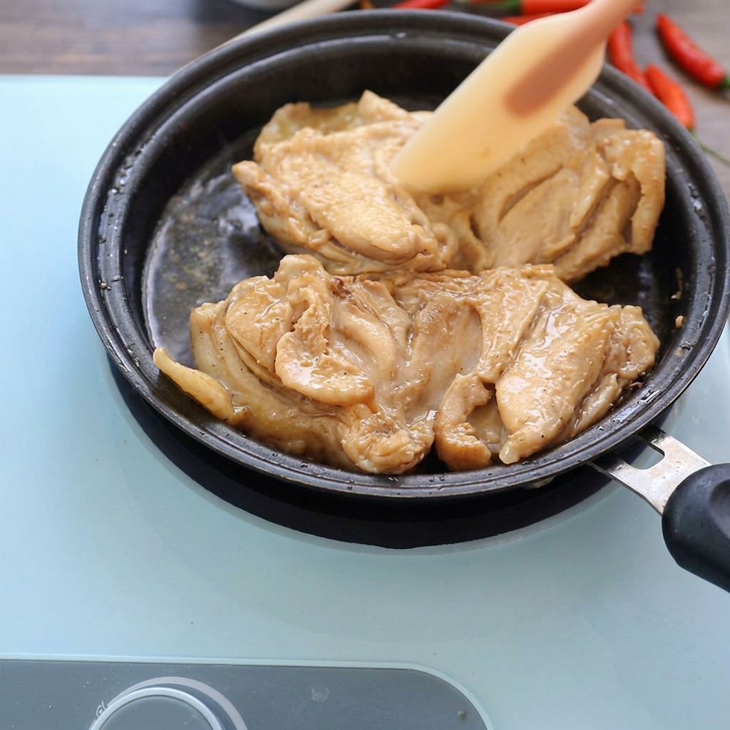 Hauts de cuisse de poulet cuits mijotant dans une poêle peu profonde avec une sauce sombre, pressés légèrement avec une spatule en silicone.