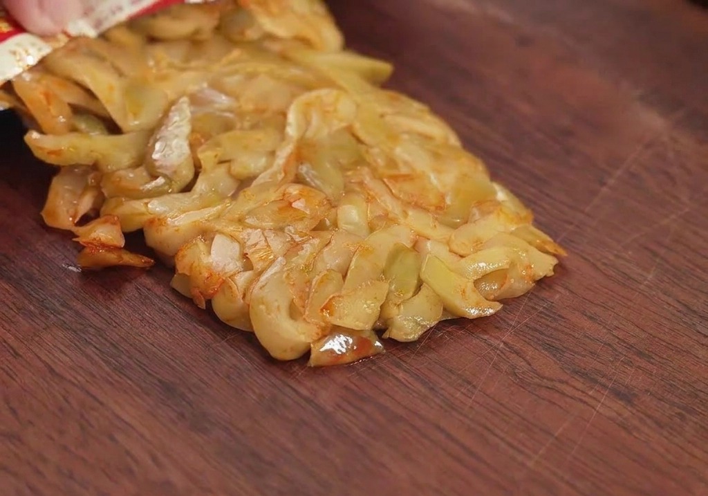 Un sachet de légumes à la moutarde conservés versé sur une planche à découper en bois, prêt à être haché.