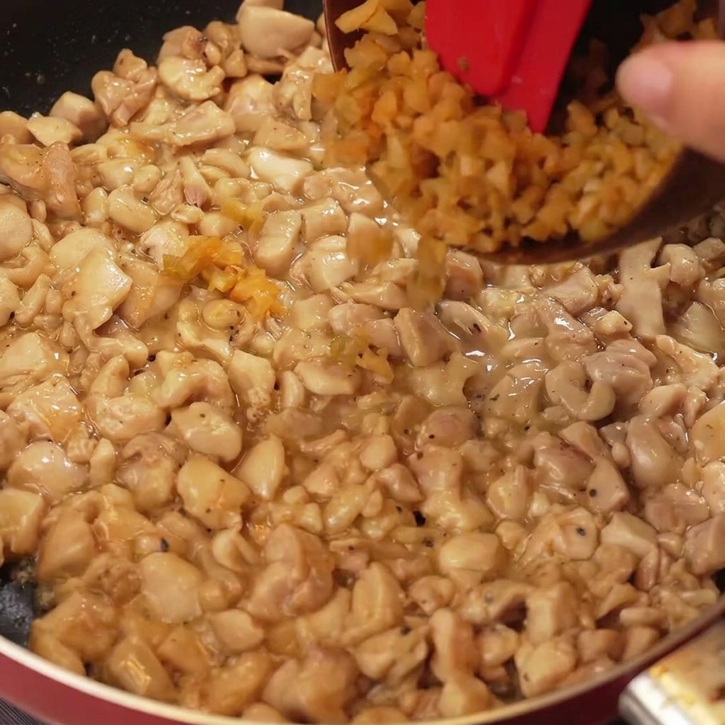 Légumes à la moutarde finement hachés et morceaux doignon blanc ajoutés dans une poêle contenant les morceaux de poulet dorés.
