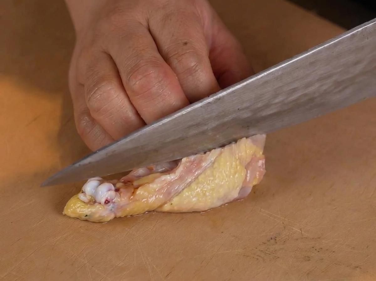 Une personne utilisant un couteau de chef pour retirer soigneusement los dune cuisse de poulet crue sur une planche à découper en bois.