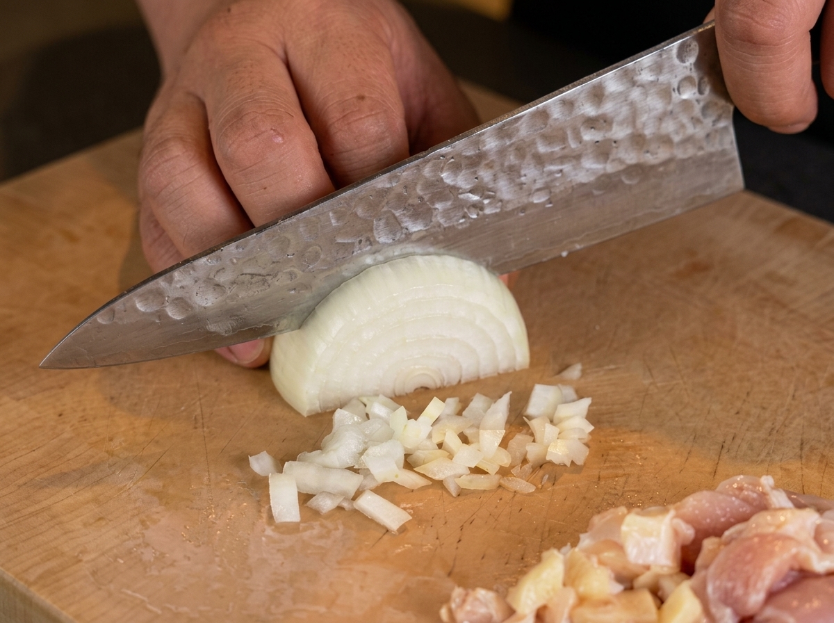La main dun chef utilisant un couteau pour hacher finement un demi-oignon blanc sur une planche.
