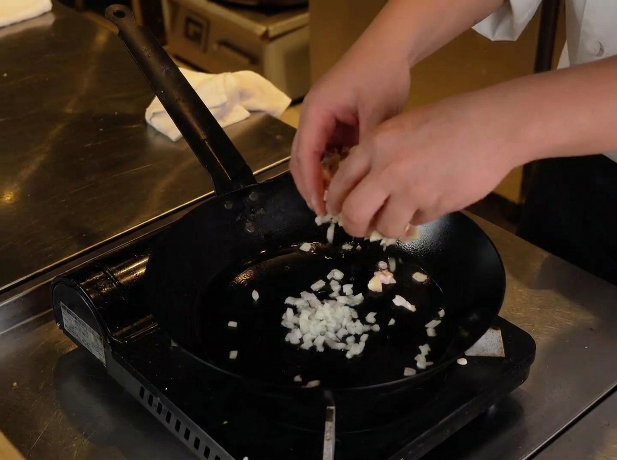 Deux mains ajoutant le poulet et le cartilage hachés dans la poêle chaude avec les oignons.
