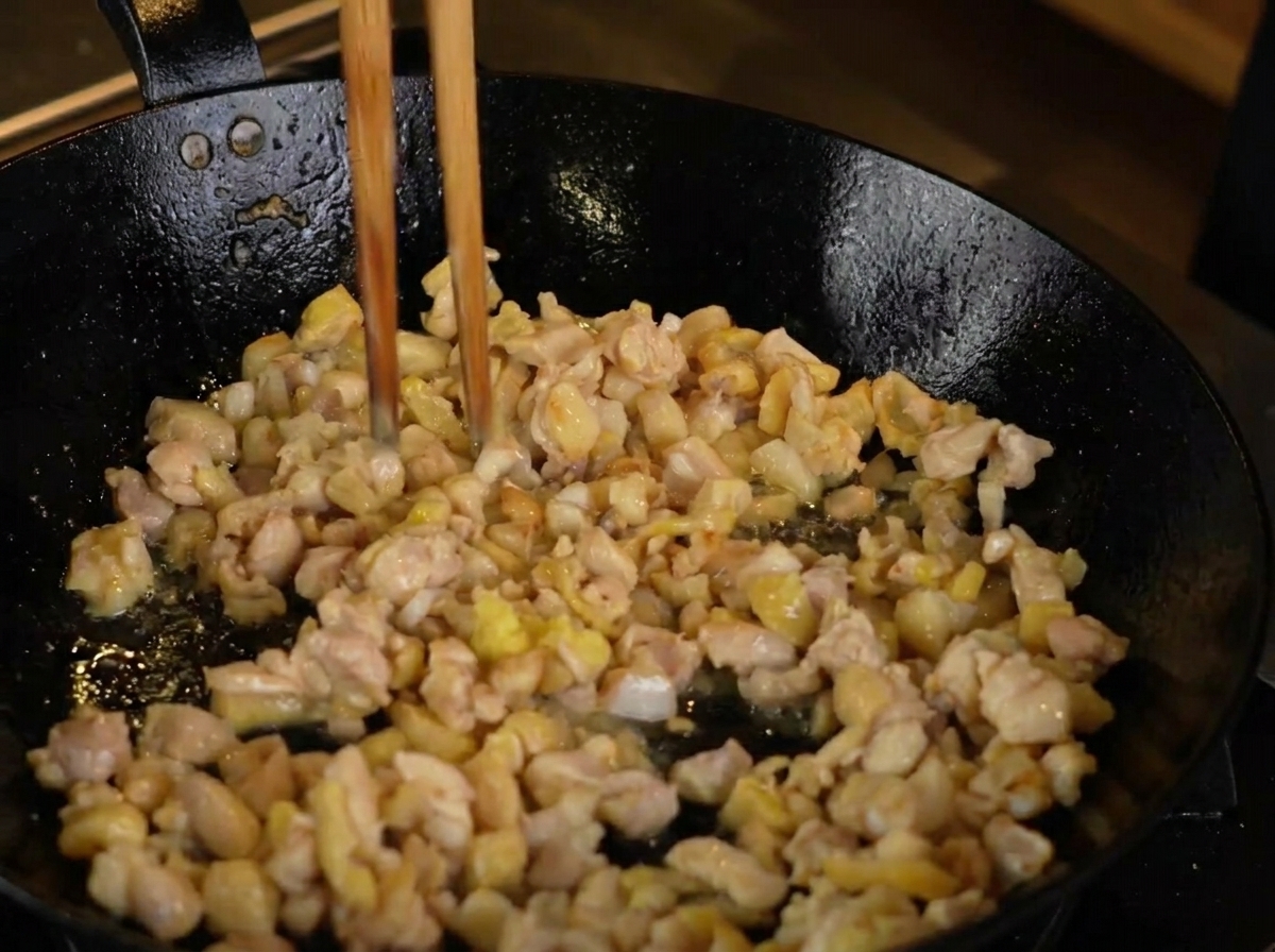 Du gingembre râpé ajouté au poulet qui dore dans une poêle chaude.