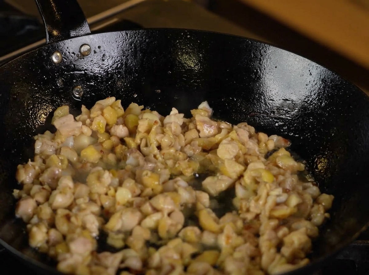 Du saké versé dans une poêle contenant le poulet et les aromates.
