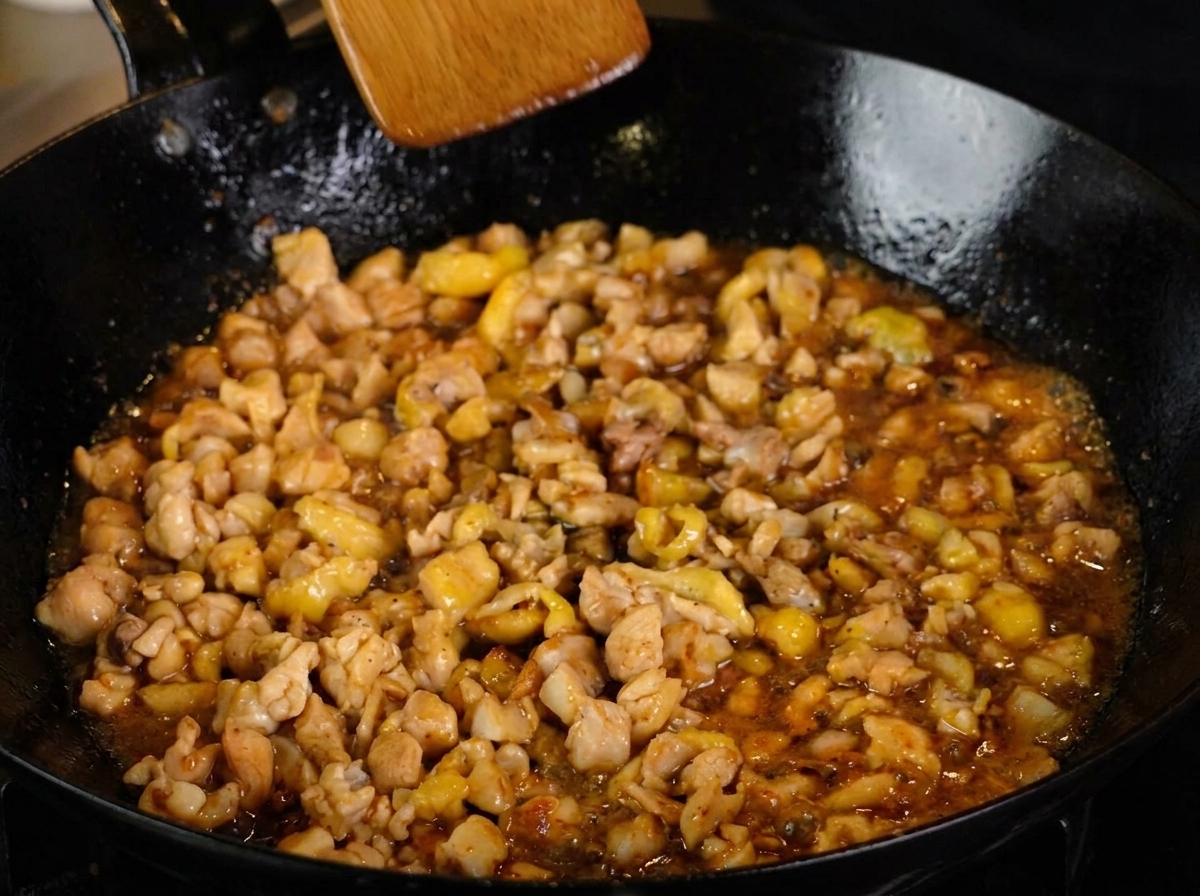 Poulet haché mijotant dans une sauce riche, saupoudré de poivre noir et mélangé avec une spatule en bois.