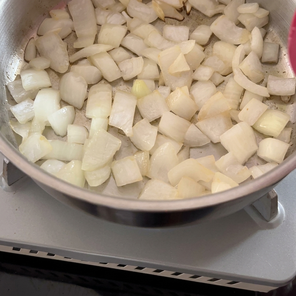 Oignons blancs hachés sautés dans une casserole en métal avec une spatule rouge.