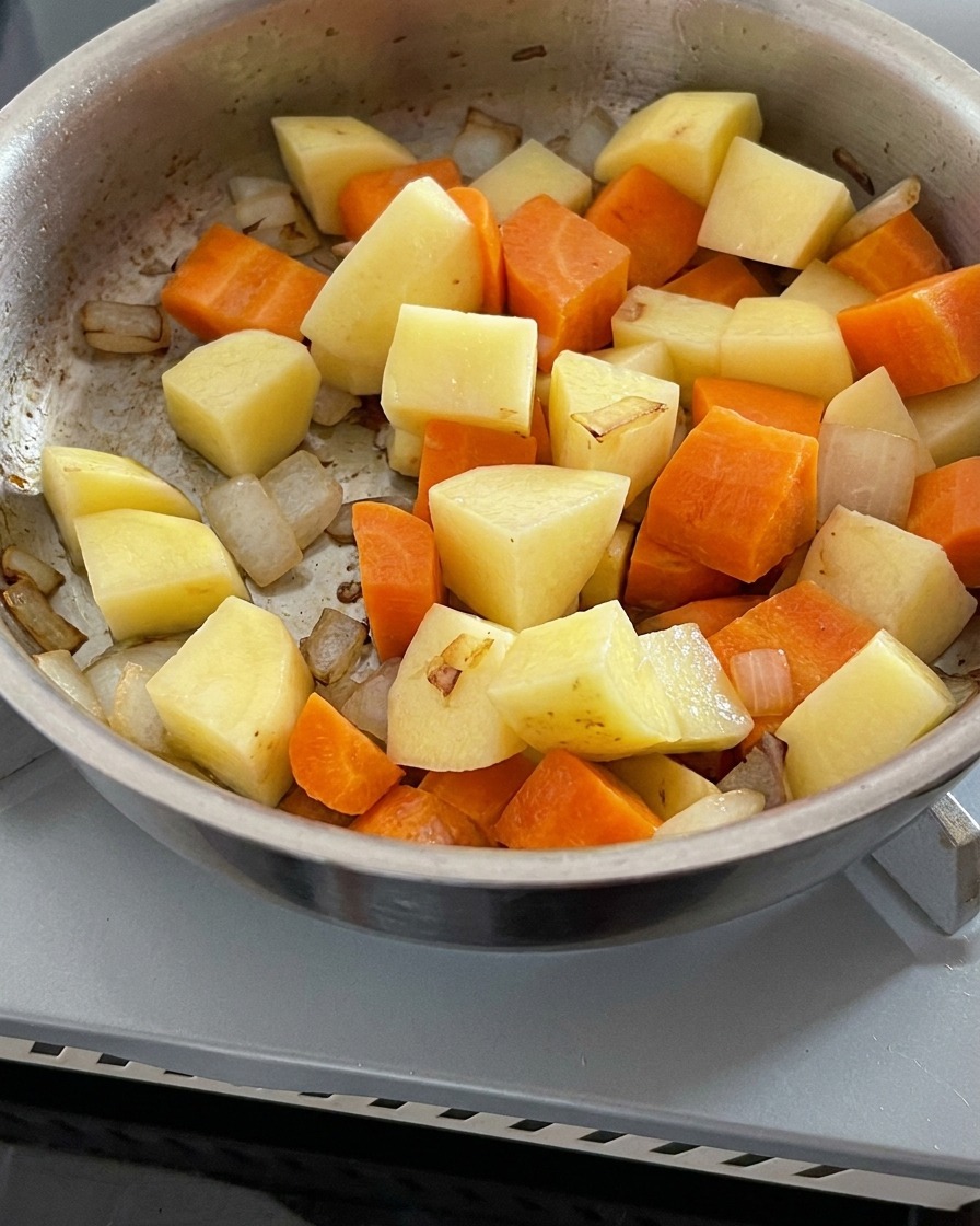 De leau claire versée dans une casserole contenant des oignons, des carottes et des pommes de terre sautés.