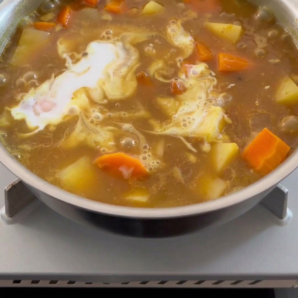 Du lait de coco onctueux versé dans une sauce au curry brune bouillonnante.