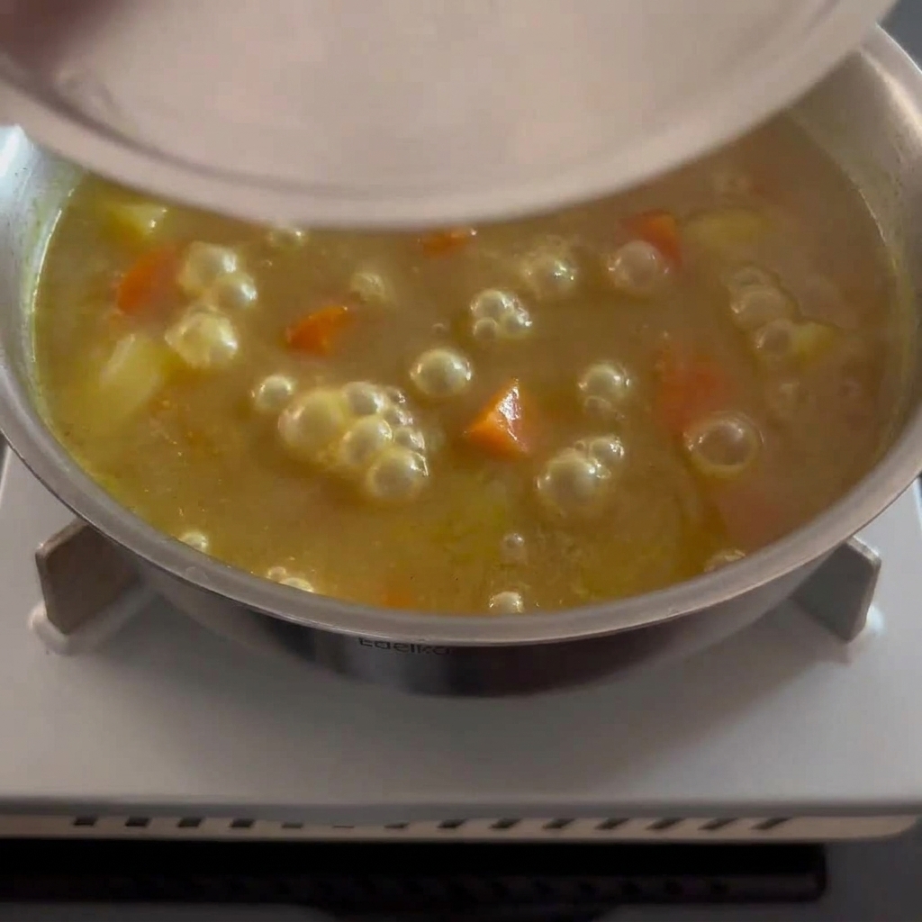 Une épaisse sauce au curry brun doré remuée avec des morceaux tendres de pomme de terre et de carotte visibles.
