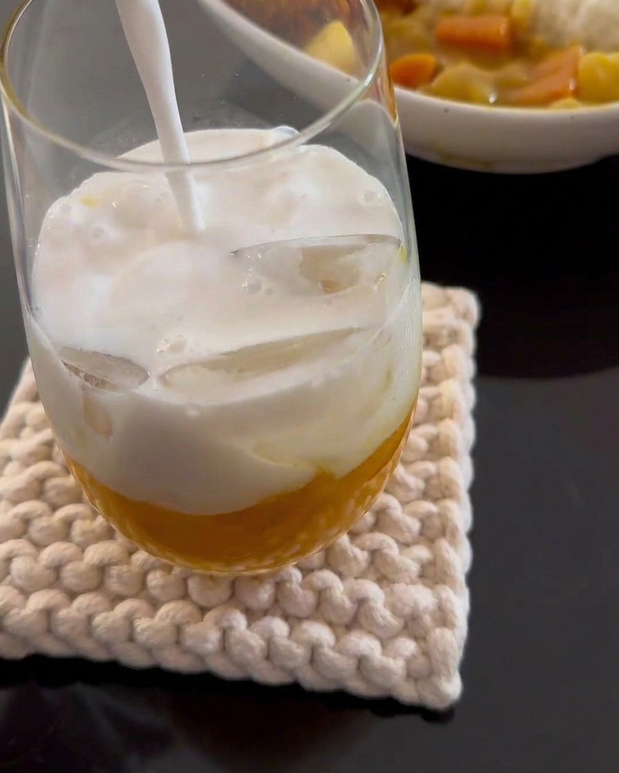 Du lait de coco blanc versé dans un grand verre contenant de la purée de mangue jaune et des glaçons.