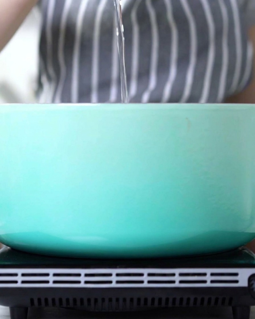 Un filet dhuile versé dans une cocotte en fonte émaillée bleu clair propre.