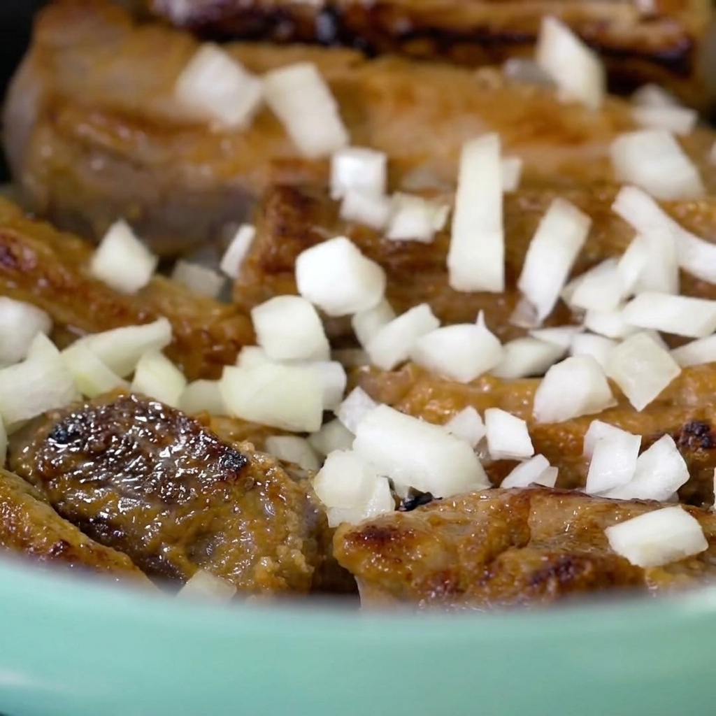 Des morceaux doignon blanc fraîchement hachés éparpillés sur les travers de porc dorés dans une cocotte bleu clair.