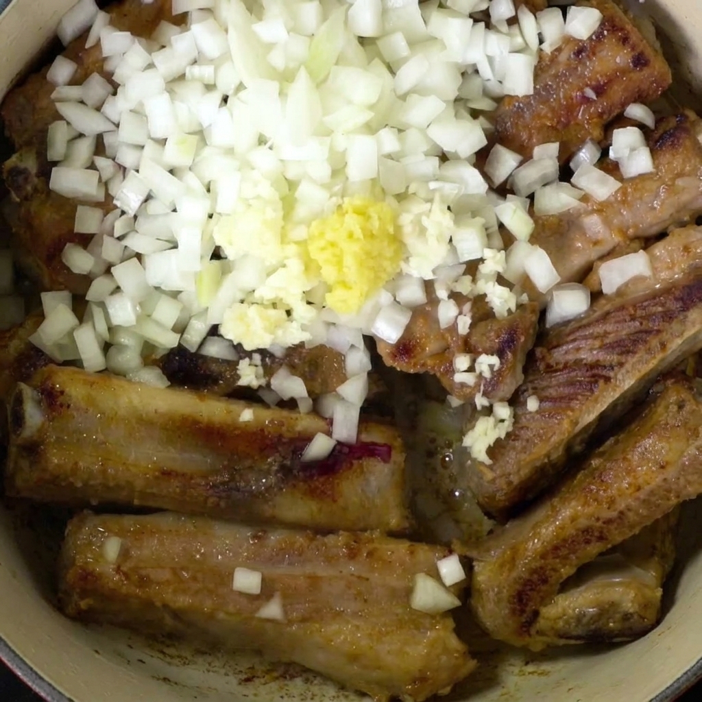 Vue de dessus de travers de porc dans une cocotte, généreusement recouverts doignons blancs en dés et dun tas de gingembre et dail émincés.