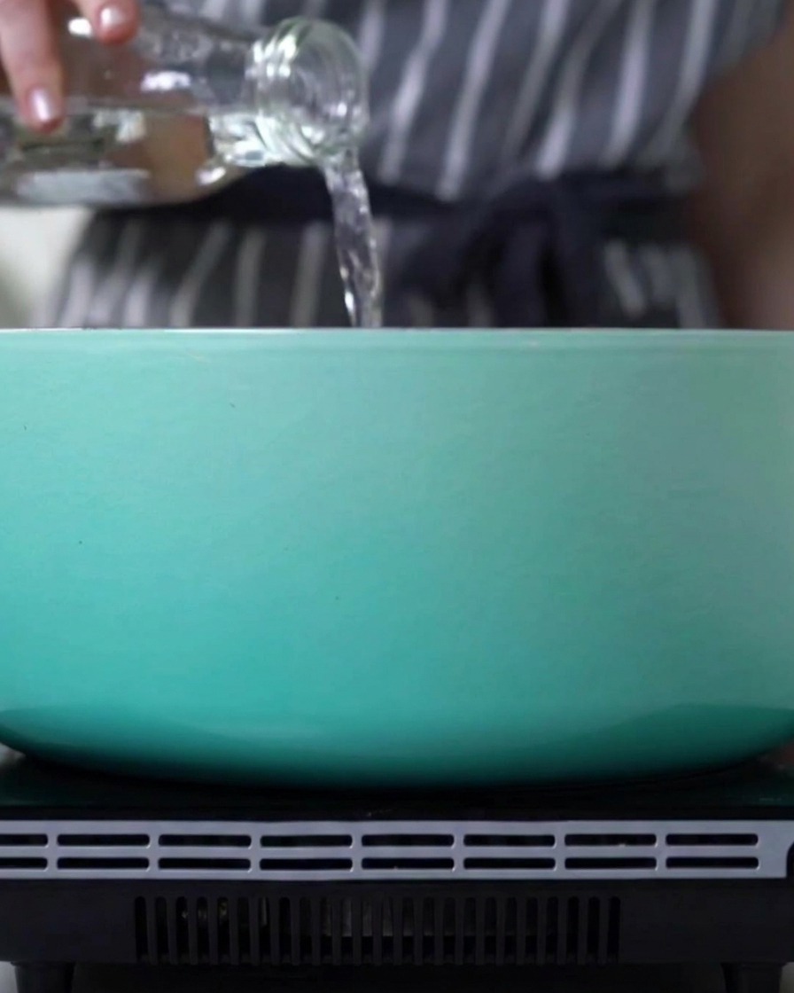 De leau versée depuis une bouteille en verre dans une cocotte bleu clair sur une cuisinière.