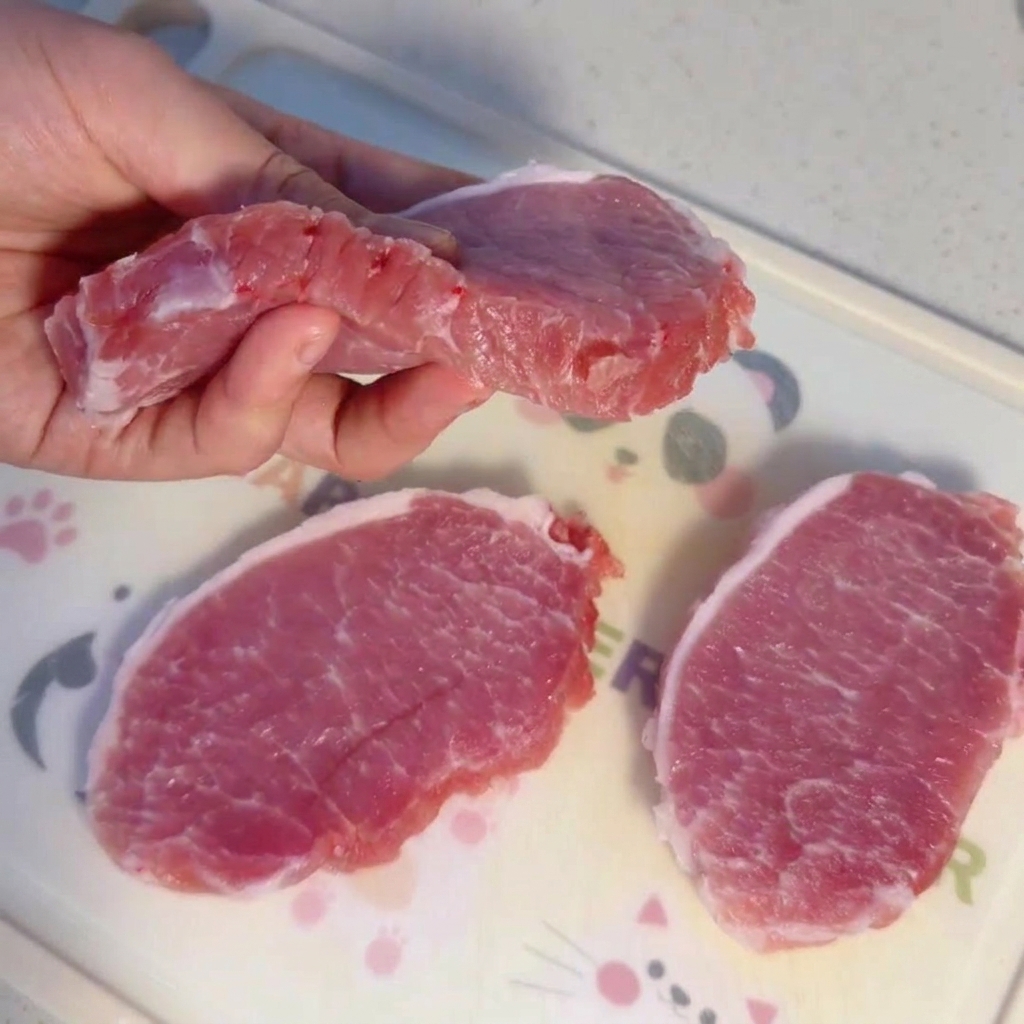 Tranches épaisses de filet de porc cru sur une planche à découper.