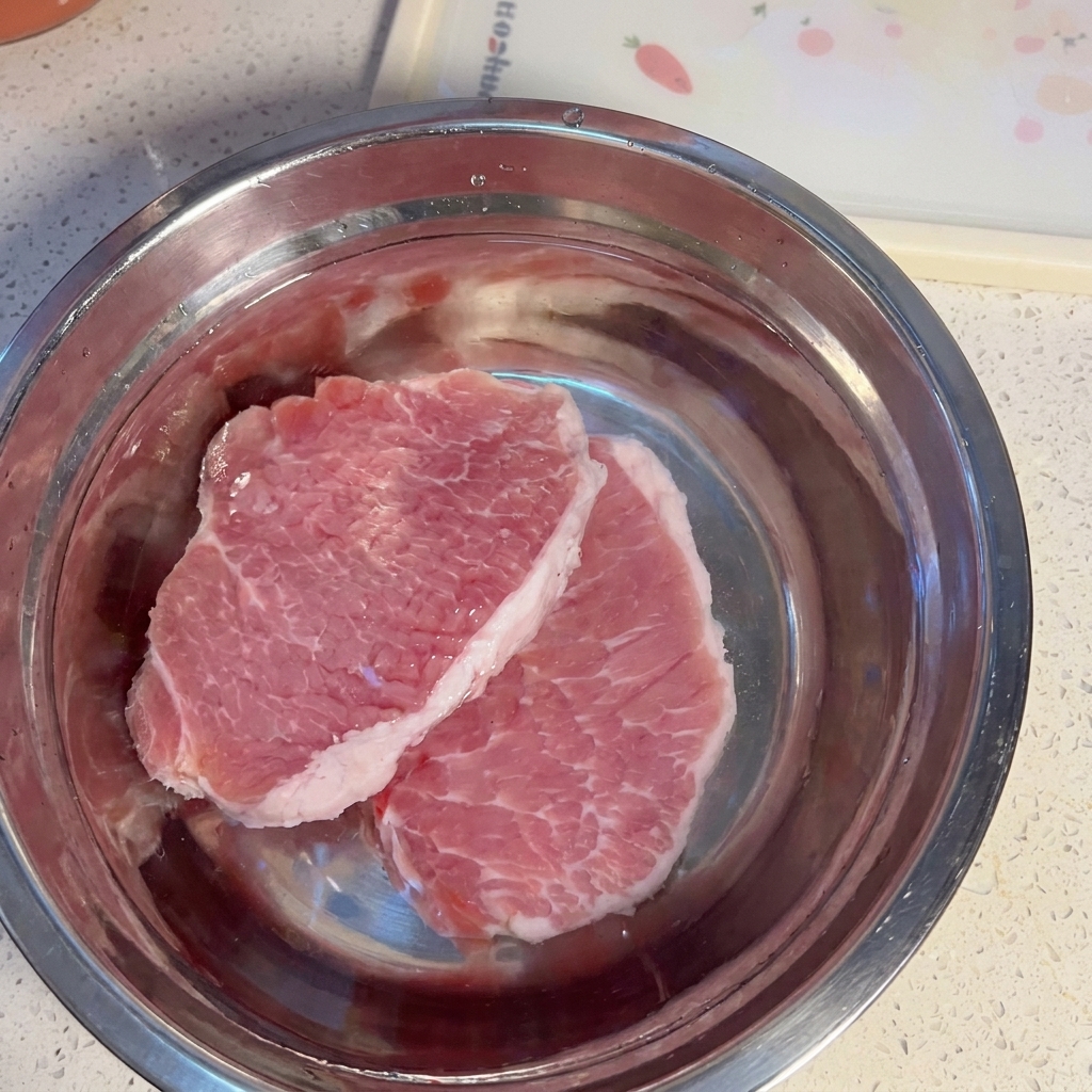 Tranches de porc cru trempant dans un bol deau.