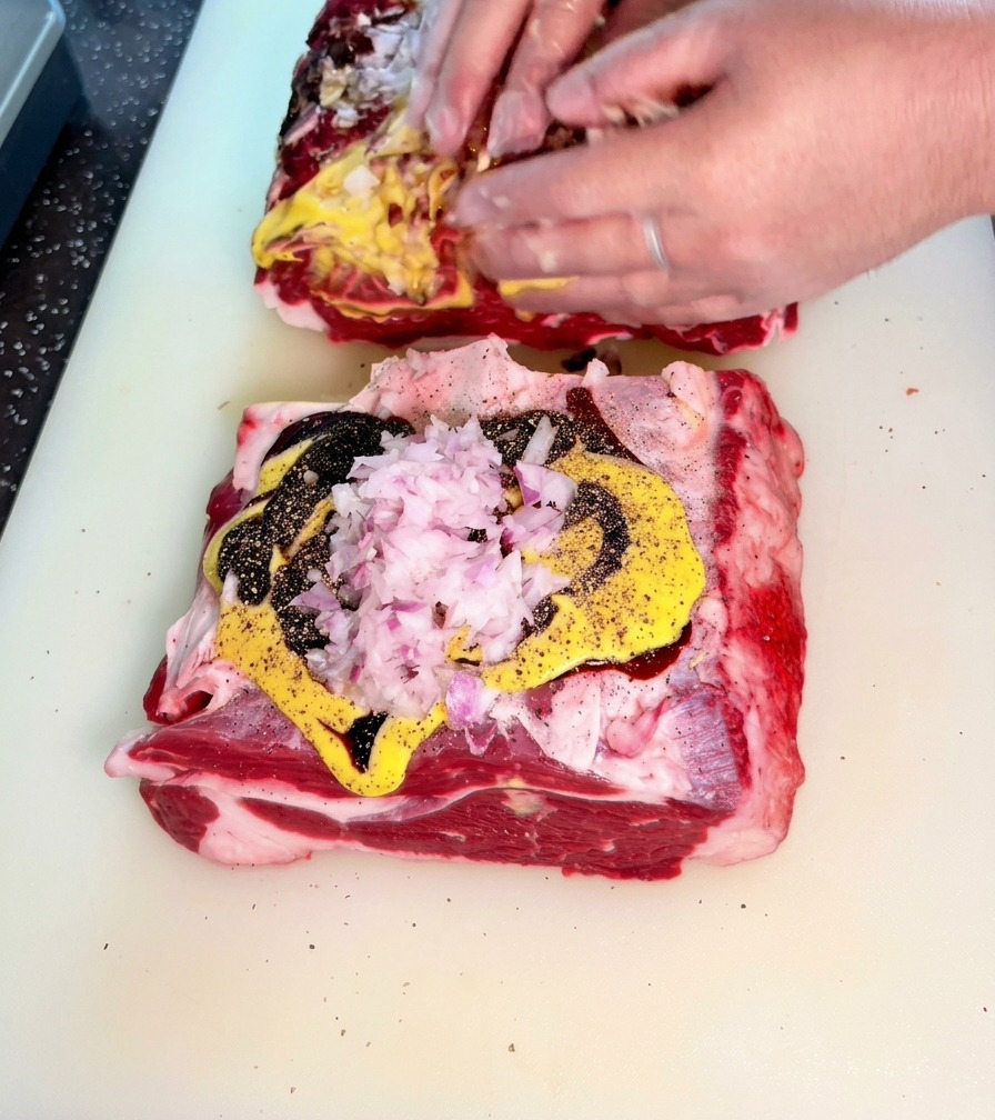Mains frottant activement un mélange doignons hachés, de moutarde et de sauces sombres sur les pièces de bœuf.