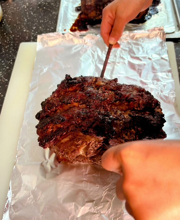 Une pointe de métal perçant la surface sombre et grillée dun gros rôti de bœuf sur de laluminium.