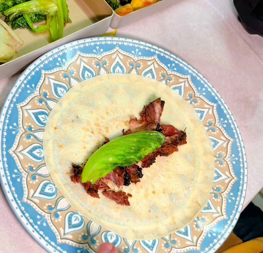 Vue de dessus dune assiette bleue avec une tortilla garnie de tranches de bœuf juteuses et dune feuille verte fraîche.