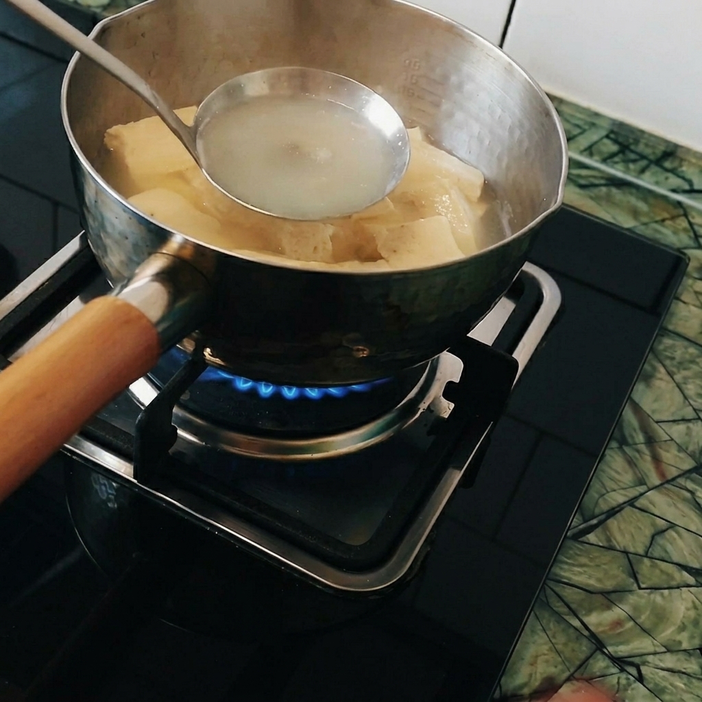 Des morceaux de curry en train de fondre dans une louche plongée dans la casserole.