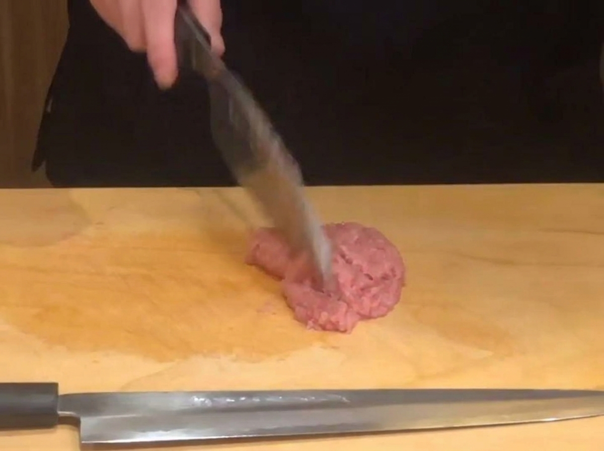 La main dun chef utilisant un couteau bien aiguisé pour hacher finement du thon cru rose sur une planche à découper en bois.