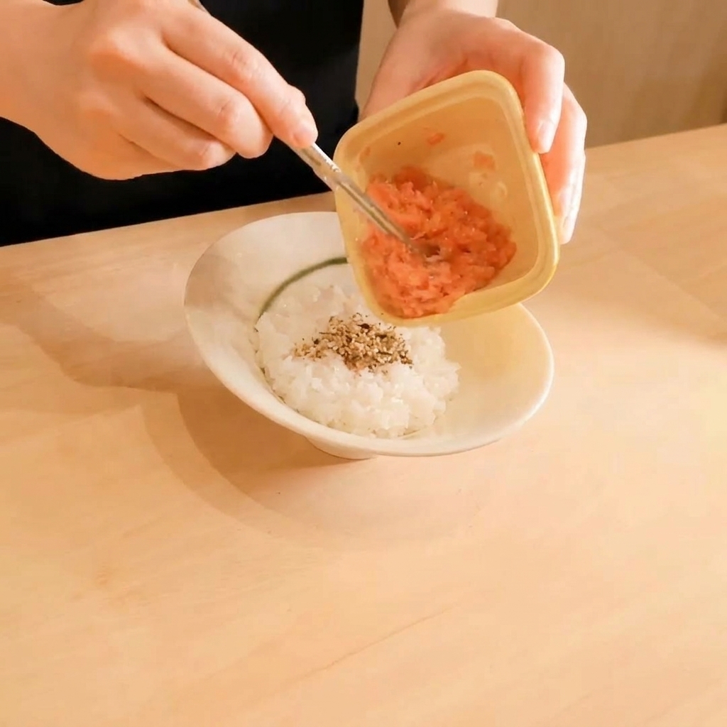 Du thon cru haché étant transféré dun petit récipient en plastique sur un lit de riz blanc parsemé de graines de sésame.