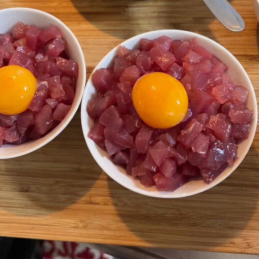 Un jaune dœuf cru bien doré trônant sur un bol de thon et de riz, garni de cébettes vertes.