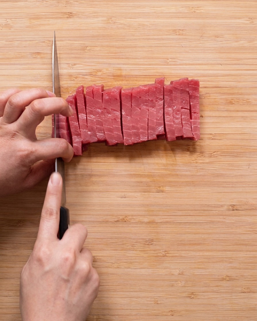 Cubes réguliers de thon rouge cru disposés sur une planche à découper en bois.