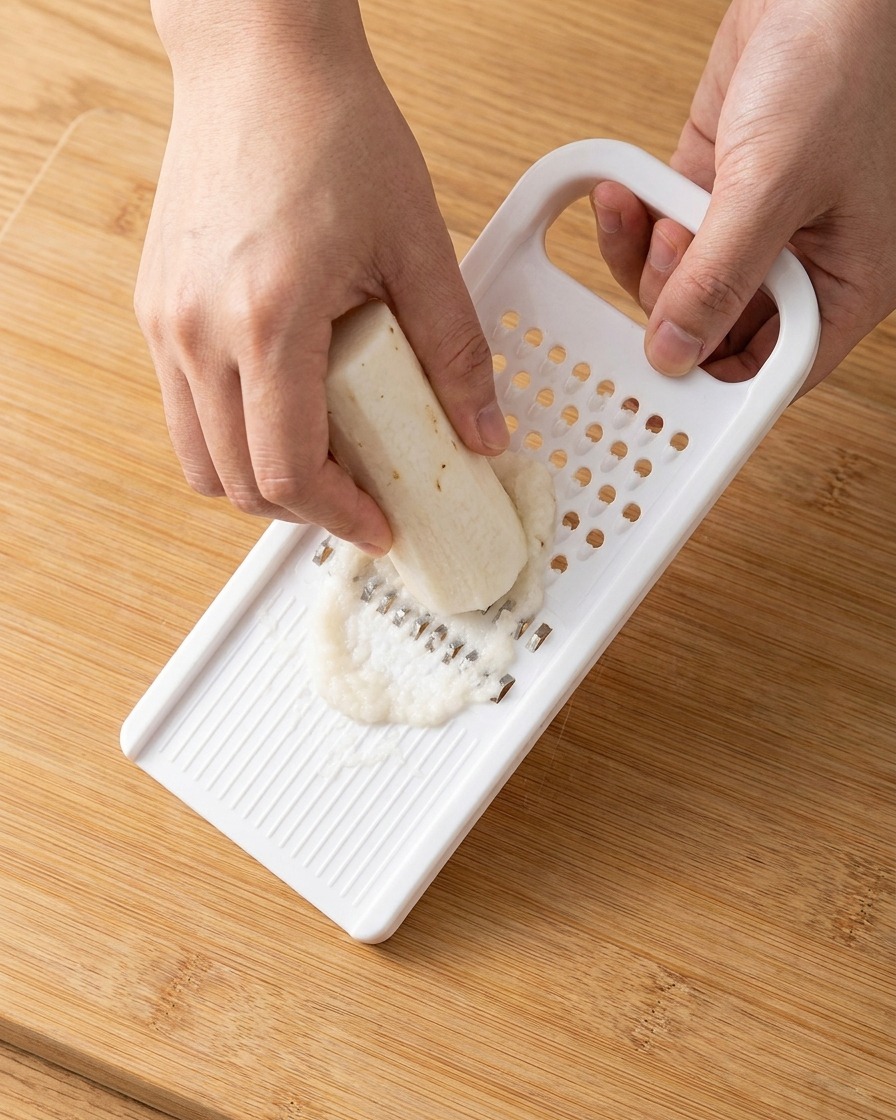Pâte digname blanche fraîchement râpée recueillie sur une râpe en plastique.