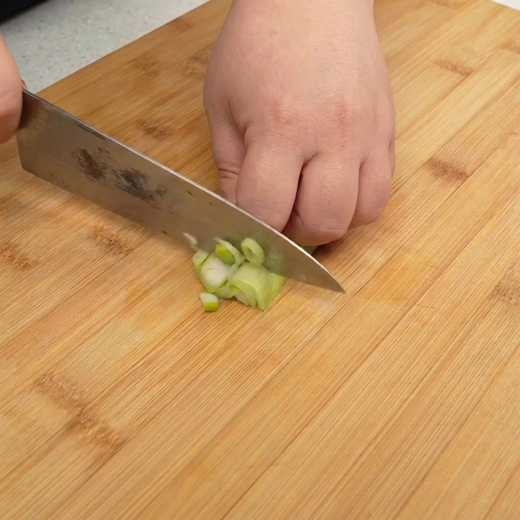 Oignons verts finement hachés sur une planche à découper en bois.