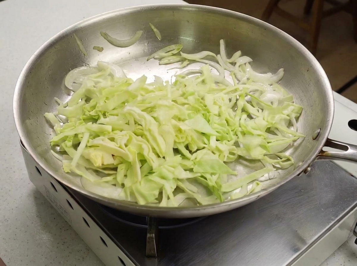 Chou vert émincé ajouté dans une poêle avec des oignons sautés.