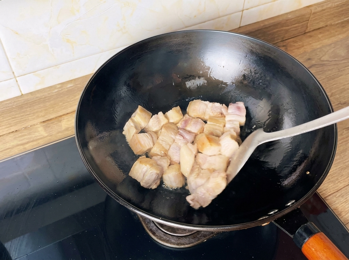 Cubes de poitrine de porc sautés dans un wok avec une spatule jusquà ce quils soient dorés.