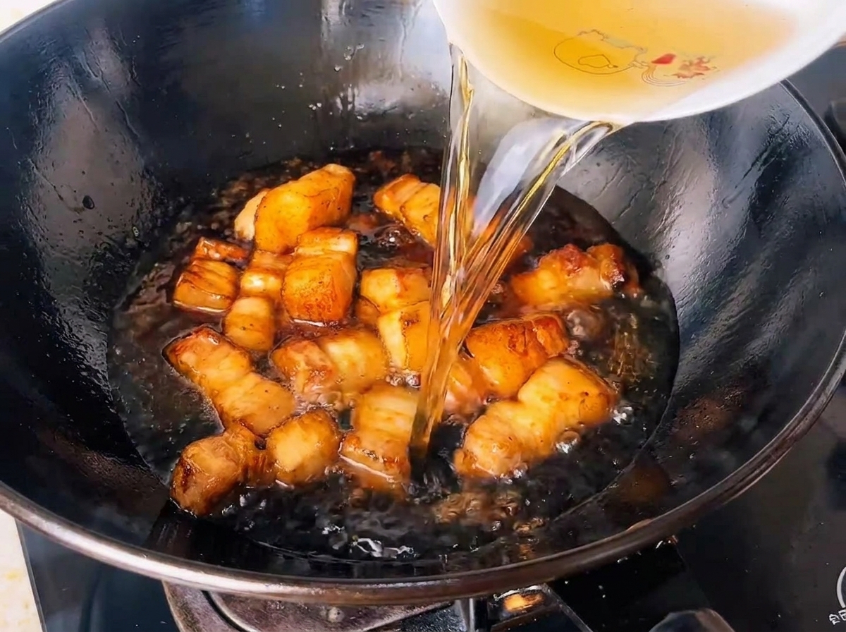 Leau de thé vert infusée versée dans un wok rempli de cubes de porc assaisonnés.