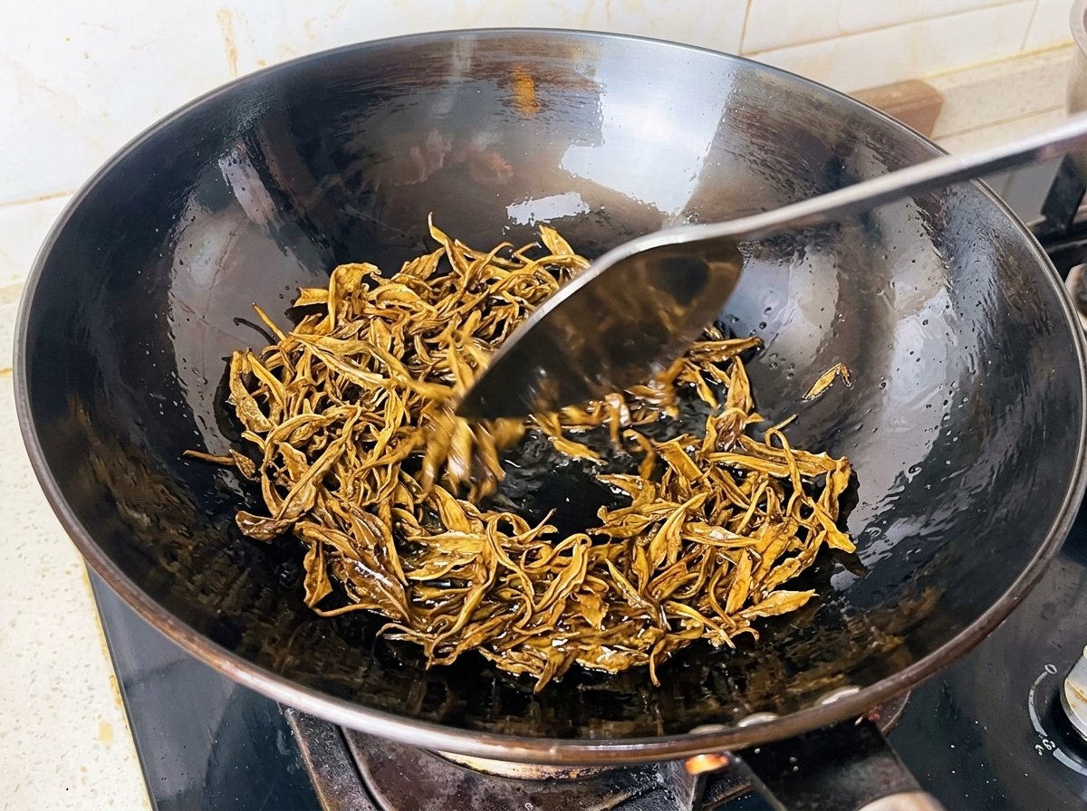 Feuilles de thé vert humides frites dans de lhuile chaude à lintérieur dun wok noir avec une spatule en métal.